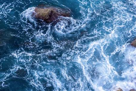Moving wave and blue water of mediterranean sea touching rock beach making some small white bubble on surface.の写真素材
