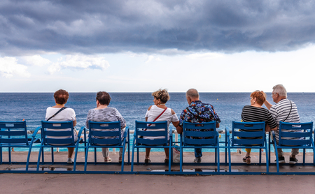Nice, France - October 1, 2018: People relaxing on public bench and looking to sea view at Mediterranean sea of Nice, France on cloudy day.のeditorial素材