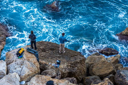 Nice, France - October 2, 2018: Men using hook for fishing fish on big rocks at Mediterranean turquoise sea in morning of Nice, France.のeditorial素材