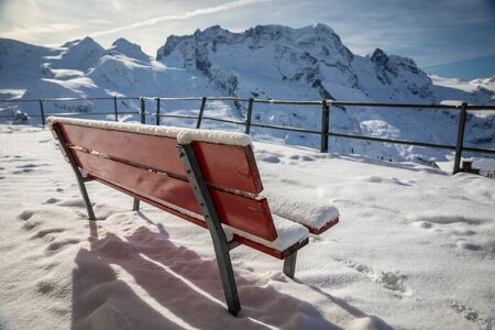Red bench and ground covered by snow on terrace for watching snowcapped mountains in Switzerland.の写真素材