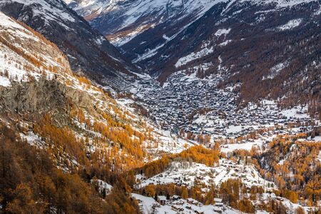 Aerial view over town of Zermatt, Switzerland, city surrounded by mountains and orange pine trees of autumn season, snow start to cover area in early winter of November, 2019.の写真素材