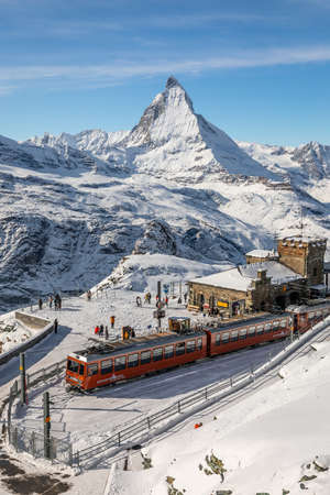 Gornergrat, Zermatt, Switzerland - November 12, 2019: Red cable car train on snowy railway at summit station with tourists and Matterhorn summit in winter.のeditorial素材