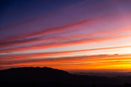 Dramatic colorful sky and clouds in pattern at sunset over silhouetted mountain range.