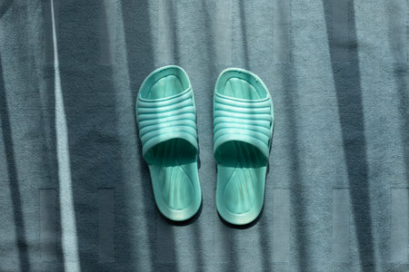 Pair of green dirty indoor plastic sandals on fluffy blue carpet with shining sunlight from window.の写真素材