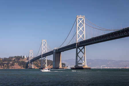 Panoramic view of boat passing through San Francisco - Oakland Bay bridge with clear blue sky.