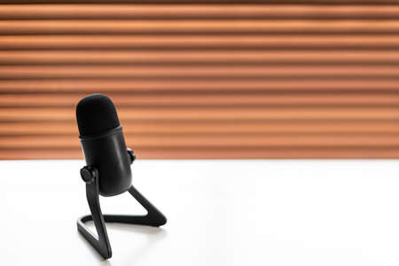 Close focus on standard black microphone on white table and space with blurry background of brown pattern backdrop.の写真素材