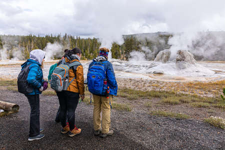 Wyoming, USA - October 1, 2019: Group of tourist on hot zone inside Yellowstone national park to watch white smoke from eruption of geysers on natural trail.のeditorial素材