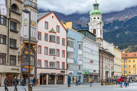 Innsbruck, Austria - November 3, 2021: Cityscape of colorful buildings with background of mountain with clouds, people walking on street for shopping and sightseeing.のeditorial素材
