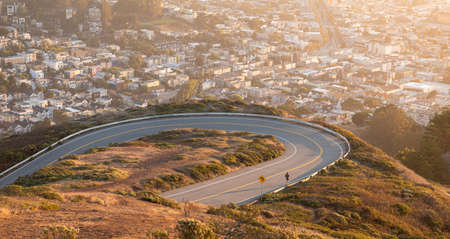 Man joking on curved road on Twin Peaks Blvd road with blurry aerial view of misty city of San...
