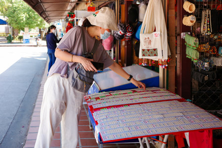 Nan, Thailand - December 5, 2022: Lady in casual dresses during travel in Thailand choosing the lucky number on lottery shelf on souvenir shop.のeditorial素材