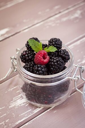 Closeup of fresh blackberries and raspberry with a mint leaf in a glass jar onの写真素材