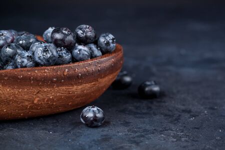 Fresh blueberries with a leaf of mint in the heart-shaped bowl on a dark blue backgroundの写真素材