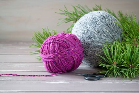 Fuchsia and grey tweed yarn on the wooden background near branches of pine-tree with black vintage...