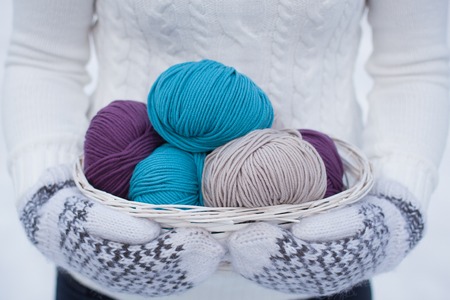 Wool yarn in a white basket. White and brown knitted wol-ol mittens. White knitted sweater background. Winter view. Snowy.の写真素材