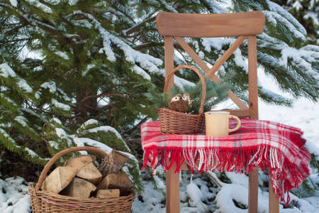 Christmas-tree toys in the basket with a cup of coffee on the wool blanket on the chair near large basketful of firewoodの写真素材