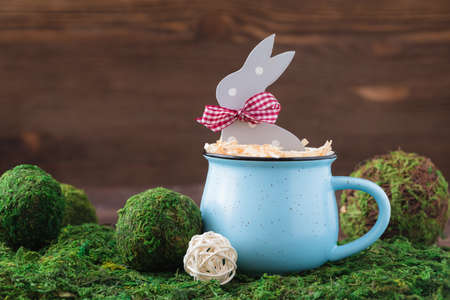 Wooden polka dot grey rabbit in a blue cup on the grass background, Easter postcard concept, tonedの写真素材