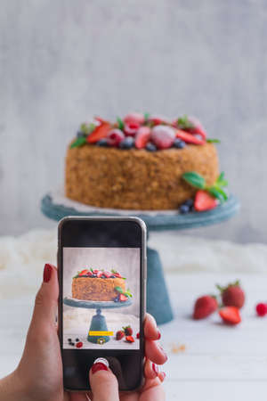 Homemade honey cake with strawberries, blueberries and raspberries on light background, toned
