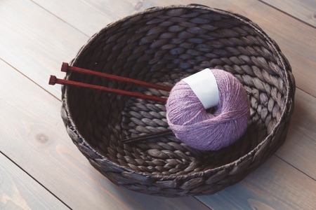 Wool yarn and knitting needles in the basket on the wooden background, toned vintage