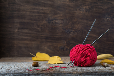 Bright red wool yarn with wooden needles among leaves and acorns, autumn knitting postcard, tonedの写真素材