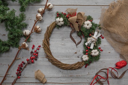 Top view of stages of making Christmas wreath with fir branches and decorative toys on wooden rustic tabletop, tonedの写真素材