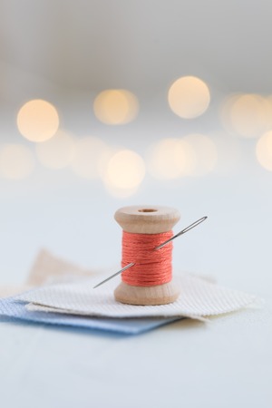 Trendy coral colored threads wooden bobbin for stitching with a needle on a white background