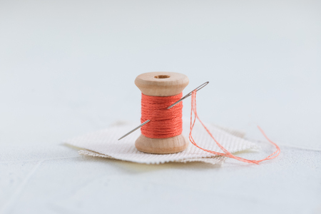 Trendy coral colored threads wooden bobbin for stitching with a needle on a white backgroundの写真素材
