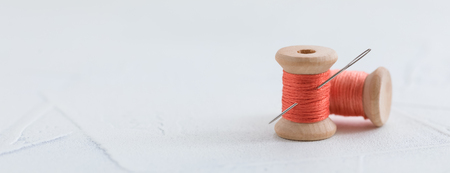Trendy coral colored threads wooden bobbin for stitching with a needle on a white backgroundの写真素材