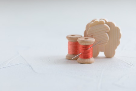 Trendy coral colored threads wooden bobbin for stitching with a needle on a white backgroundの写真素材
