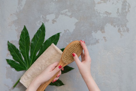 zen detox still-life - body spa treatment bamboo brush on green tropical leaf, concrete background