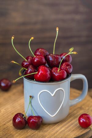 Fresh cherries in grey heart shaped cup on wooden table, toned