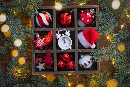 Christmas red and white glass toys, alarm clock, santa claus hat in the basket with fir tree branches background, sparkling garlandの写真素材