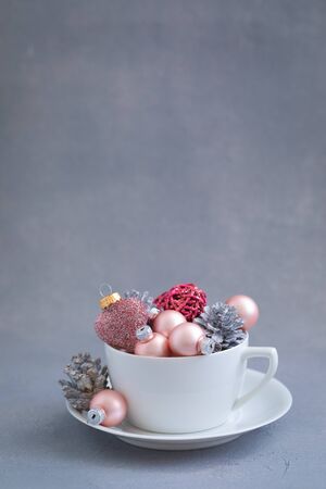 Pink christmas balls and natural cone in the white tea cup on grey background with snowflakes, invitation. holiday menu, postcard conceptの写真素材
