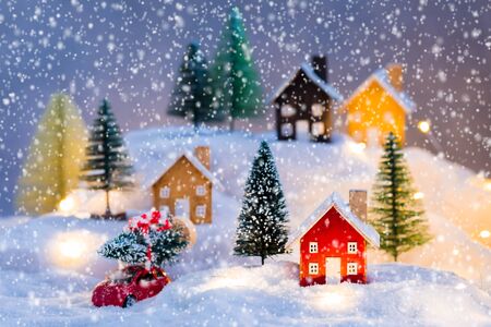 Miniature wooden houses village over blurred Christmas decoration background, with red car and toy fir trees property real estate investment greetings conceptの写真素材