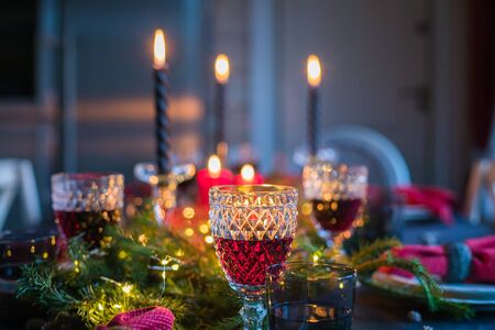 Table served for Christmas dinner, festive setting with decorations, burning candles and fir-tree branches, glassesの写真素材