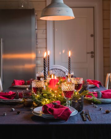 Table served for Christmas dinner, festive setting with decorations, burning candles and fir-tree branches, glassesの写真素材