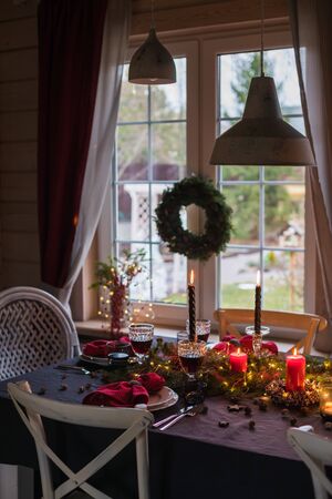 Table served for Christmas dinner, festive setting with decorations, burning candles and fir-tree branches, glassesの写真素材
