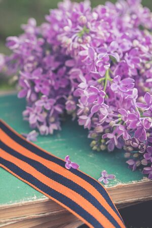 St. George ribbon on old books background with fresh lilac branch, symbol of Victory Day May 9, tonedの写真素材