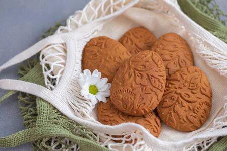Easter egg shaped ginger cookies on the kitchen towel in the mesh net bag backgroundの写真素材