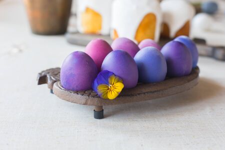 Naturally dyed hen's eggs with a violet flower on linen background, Easter spring greeting postcard...