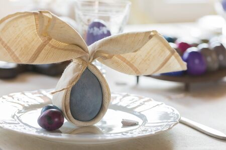Easter festive spring table setting decoration, bunny ears shaped napkins, dyed hen's and quail eggs, wooden hearts, family dinner or breakfast conceptの写真素材