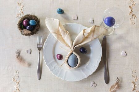 Easter festive spring table setting decoration, bunny ears shaped napkins, dyed hen's and quail eggs, feathers, wooden hearts, family dinner or breakfast conceptの写真素材