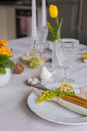 Easter festive spring table setting decoration, eggs in nest, fresh yellow tulips in vase,...
