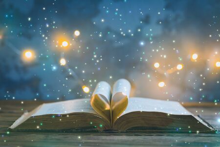 Old opened book, heart shaped paper sheets, dark background with stars and lights, World Book Day, Teachers Knowledge Day, astrology, astronomy and mystery concept, toned vintageの写真素材