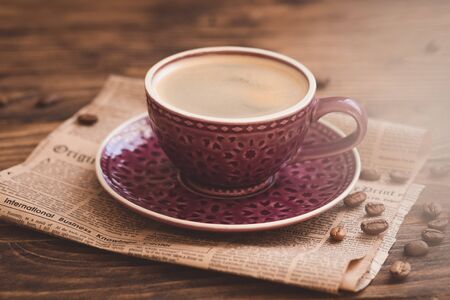 Nice purple cup of coffee with beans on newspaper background, selective focus, toned vintageの写真素材