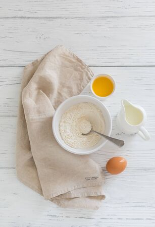 Ingredients for baking pancakes, butter, flour in white bowl, milk on wooden backgroundの写真素材