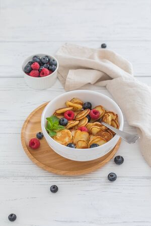 Breakfast white bowl with tiny pancake cereal with blueberries, raspberries and mint on wooden backgroundの写真素材