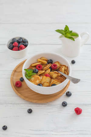 Breakfast white bowl with tiny pancake cereal with blueberries, raspberries and mint on wooden backgroundの写真素材
