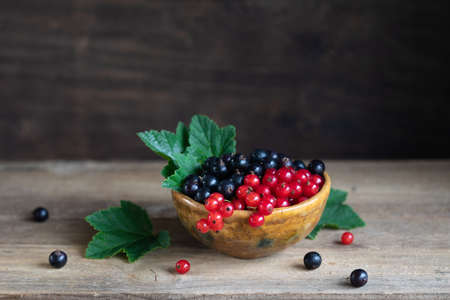 Red and black currant berries in ceramic bowl on a wooden background, toned vintageの写真素材