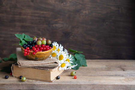 Red and black currant berries in ceramic bowl and old book on a wooden background,cottagecore lifestileの写真素材