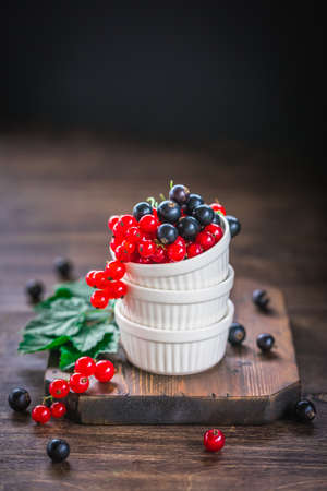 Red and black currant berries in ceramic bowl on a wooden background, toned vintage